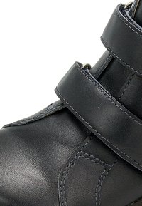 Stivaletto in pelle nera con due chiusure a cinturino regolabili, texture morbida e dettaglio di cucitura a contrasto sui lati.