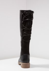 Černé kožené boty po kolena s tkaničkami vzadu, hladká kožená podrážka, semišový svršek a hnědočerná gumová podrážka s nízkým podpatkem, zobrazené zezadu.