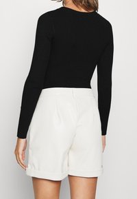 Zwarte geribde lange mouw top gecombineerd met witte op maat gemaakte shorts met een omgeslagen zoom. De outfit heeft een aansluitende silhouet en een gladde textuur.