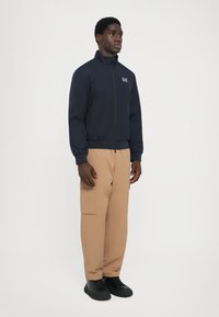 Navy bomber jacket with a zip front and ribbed cuffs, paired with beige cargo pants featuring side pockets, and black lace-up shoes.