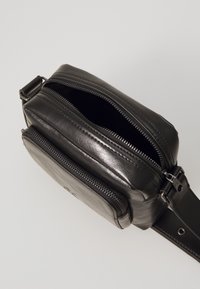 Čierna kožená crossbody taška so zipsom na dvoch oddeleniach, textúrovaným povrchom a odnímateľným popruhom. Kompaktný obdĺžnikový tvar.