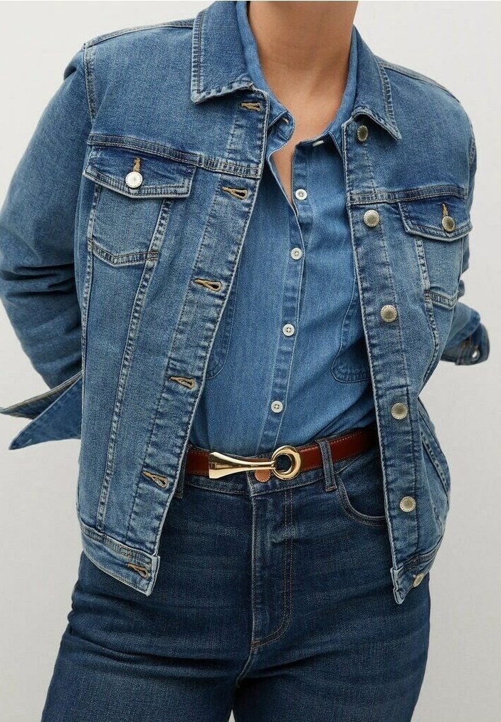 Chaqueta de denim en azul claro con bolsillos con botones, un cuello clásico y detalles de metal plateado, combinada con una camisa de botones azul y un cinturón marrón.
