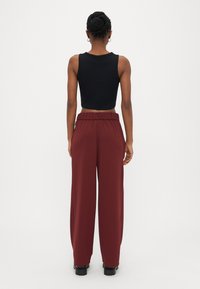 Top corto negro sin mangas combinado con pantalones de pierna ancha color burdeos, con una cintura elástica y textura suave. Vista trasera del conjunto.