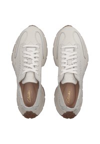 Zapatillas blancas de cuero con acentos texturizados, lados elásticos y cordones planos. Suelas de goma marrón con un diseño curvado. Marca dorada en el interior.