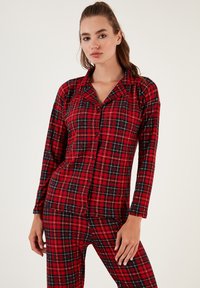 Conjunto de pijama a cuadros rojos que incluye una parte superior de botones de manga larga y pantalones a juego con acentos en negro y azul. Tejido suave con patrón de cuadros.