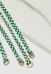 Gröna och vita mönstrade remmar med guldfärgad hårdvara, fästa vid ett krämfärgat tyg med en slät yta och platt design.