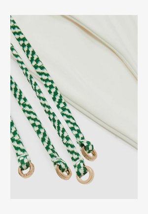 Grüne und weiße gemusterte Riemen mit goldenen Beschlägen, befestigt an einem cremefarbenen Stoff, der eine glatte Textur und flaches Design aufweist.