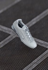 Heledad hallhalli Nike'i tossud lipsudega, millel on swooshi logo, asetatud tekstureeritud metallresti pinna kohale.