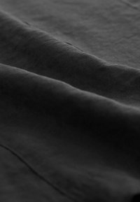 Tissu noir texturé avec des surfaces douces et lisses et des reflets subtils, présentant de doux plis et des nuances variées à la lumière.