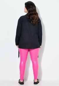 Schwarzes Langarmshirt mit einem geknöpften Bund, kombiniert mit glänzenden rosa Leggings und flachen schwarzen Schuhen mit goldenen Akzenten.