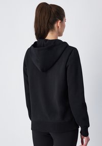 Felpa nera con cappuccio, realizzata in tessuto morbido, presenta un grande cappuccio, maniche lunghe e una vestibilità rilassata con polsini e orlo a coste.
