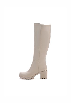 Bota beige hasta la rodilla hecha de material suave con un tacón ancho, puntera redondeada y suela con tacos. Presenta detalles de costura mínimos.