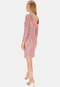 Różowa sukienka z cekinami, z dekoltem w kształcie koca i długimi rękawami, z niskim krojem pleców. Noszona z beżowymi szpilkami na kostkę.