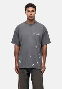 Przyduża szara koszulka z bawełny z okrągłym dekoltem, wyblakły wzór i białe plamy farby na przodzie i rękawach.