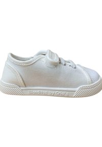 Zapatilla de lona blanca con suela de goma texturizada, puntera redondeada y diseño de cordones. Presenta una marca en el lateral y un cuello acolchado.