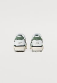 Balti ir žali sportbačiai su tinklo viršumi, zomšo akcentais ir tekstūruota guma. Ant kulno yra pilkas logotipas.