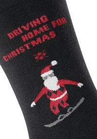 Czarna skarpeta z motywem bożonarodzeniowym: Mikołaj w czerwonym garniturze snowboardujący, z napisem "WRACAM DO DOMU NA ŚWIĘTA" w czerwonym kolorze.