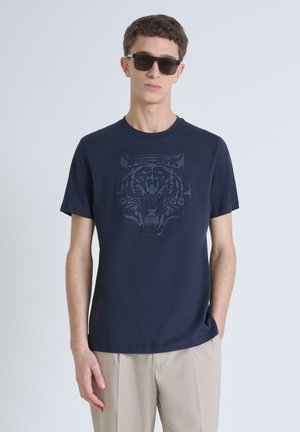 Camiseta de algodón en color navy con un gráfico de tigre negro tonal en el frente, de mangas cortas y con cuello redondo, combinada con pantalones beige claros.