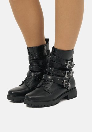 Botas de tobillo negras con un acabado de cuero mate, que cuentan con tres correas ajustables con hebillas plateadas y una cremallera lateral, suela robusta con relieve.