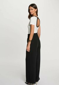 Top bianco a maniche corte con dettaglio sulla schiena aperta nero, abbinato a pantaloni neri a vita alta e a gamba larga. Il modello indossa un bracciale a manchetto e un anello.