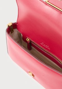 Roza usnjena torbica z zlatim okovjem, ki ima zadrgo in gladko teksturo. Notranjost je bež in prostorna.