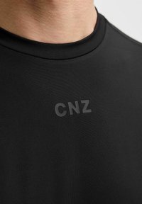 Schwarzes Kurzarmshirt mit geripptem Rundhalsausschnitt, das ein matt schwarzes 'CNZ'-Logo auf der Brust trägt und aus einem glatten, dehnbaren Material gefertigt ist.