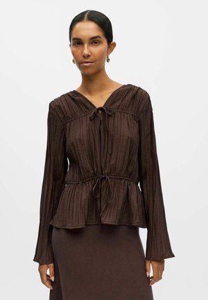 Blouse marron texturée avec un décolleté en V et un détail à nouer, manches longues et taille peplum. Présente des plis verticaux sur tout le tissu.