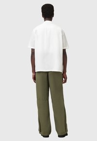 Chemise blanche à manches courtes ample avec un ourlet droit, assortie à un pantalon large olive avec des zips sur les côtés.