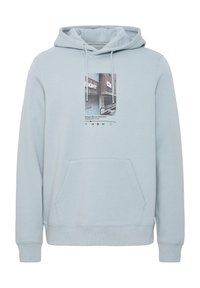 Sudadera de color azul claro, fabricada en un tejido suave, con un bolsillo frontal y una impresión gráfica que muestra imágenes urbanas y botones de reproducción.