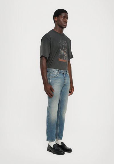 Gray graphic t-shirt with short sleeves, blue tapered denim jeans, white socks, and black loafers. Minimalistic design with faded accents.