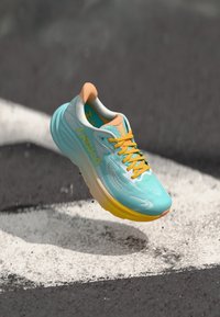 Light blue running shoe with a textured upper, yellow laces, and orange accents. Features a thick, cushioned sole for comfort.