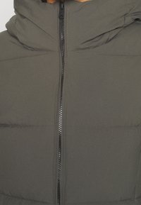 Tummanharmaa toppatakki, jossa on korkea kaulus ja etuvetoketju. Kangas näyttää sileältä, ja siinä on vaakasuorat tikatut osiot.