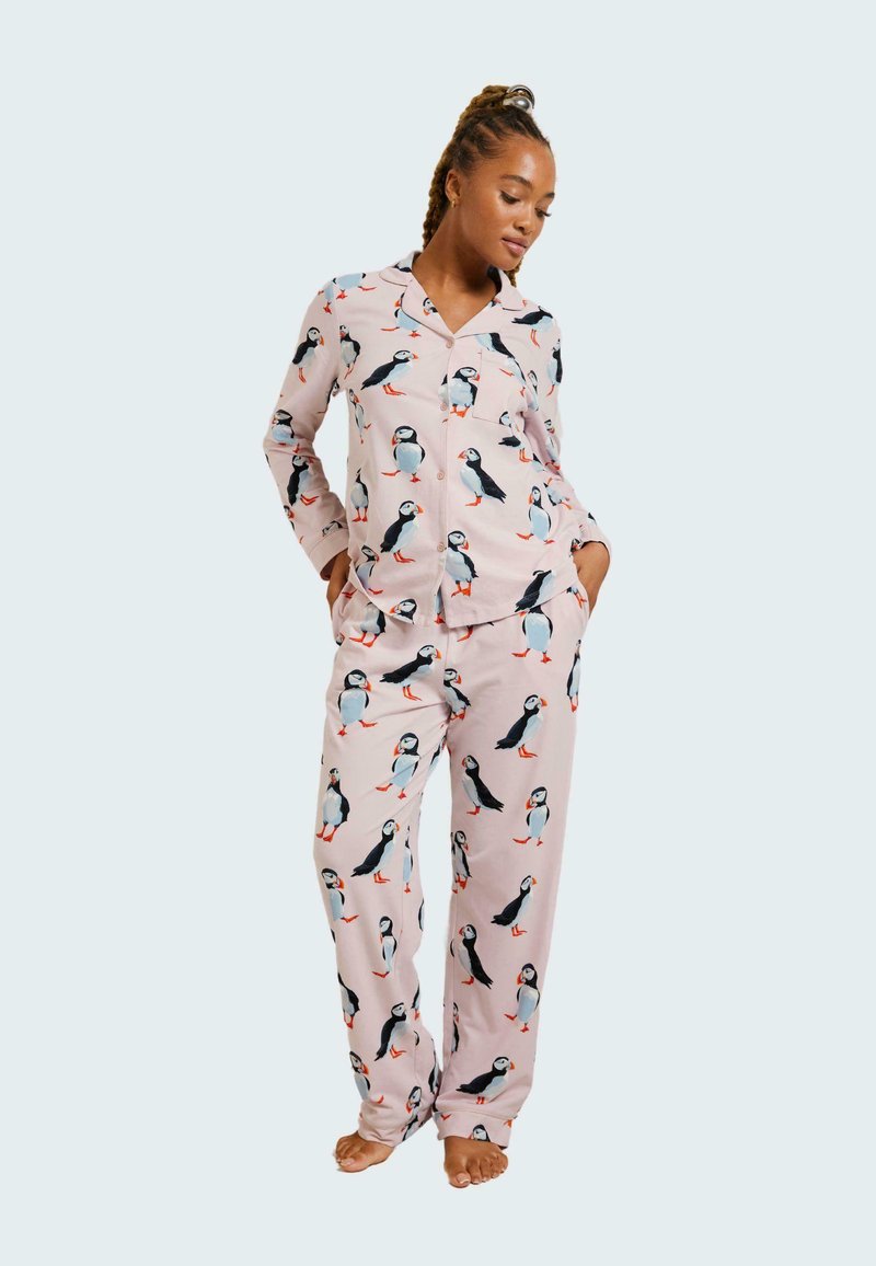Rosa pyjamasett med ett upprepat pingvinmönster, tillverkad av mjukt tyg. Topp med krage och bröstficka, matchande avslappnade byxor.
