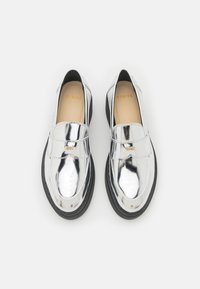 Scarpe in pelle verniciata argento con punta rotonda e suola in gomma nera. Presentano una fascia decorativa sulla parte superiore. Nome del marchio visibile all'interno.