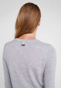 Vaaleanharmaa ribbivyötiö, jossa on pyöreä kaula-aukko, takana pieni brändilogo, sileä pinta ja pitkät hihat.