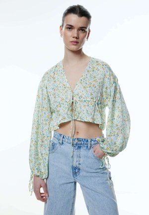 Gestreifte Bluse in einem hellen Blumendruck mit langen Puffärmeln, Bindeband und einem gerüschten unteren Rand, kombiniert mit hochtaillierten Jeans.