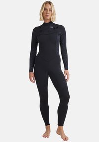 Svart våtdräkt med långa ärmar, med texturerade mönsterpaneler på sidorna, dragkedjestängning fram och förstärkt knäskydd.