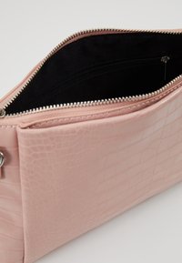 Růžová, texturovaná taška z umělé kůže s uzavíráním na horním zipu. Interiér má černou podšívku a malou kapsu na zip pro organizaci.