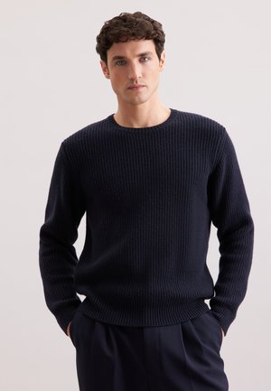 Maglione a coste blu navy con scollatura rotonda e maniche lunghe, caratterizzato da un motivo testurizzato e una vestibilità rilassata. Abbinato a pantaloni scuri.