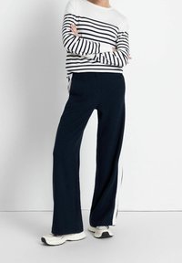 Marineblauwe broek met wijde pijpen en witte zijstrepen, gecombineerd met een wit en marineblauw gestreept shirt met lange mouwen. Zachte stof, losse pasvorm en een ronde hals.