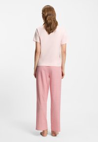 Ροζ ανοιχτό μπλουζάκι με κοντά μανίκια και στρογγυλή λαιμόκοψη, συνδυασμένο με κόκκινο παντελόνι πιτζάμας με κορδόνι στη μέση και γεωμετρικό μοτίβο. Απαλή υφή υφάσματος.