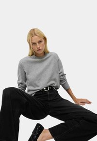 Szary sweter z okrągłym dekoltem, wykonany z miękkiego materiału, zestawiony z czarnymi spodniami o szerokim kroju i czarnymi butami wsuwanymi z ćwiekami, stylizowany w luźnym stylu.