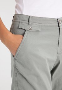 Jasnoszare spodnie o gładkiej, teksturowanej tkaninie. Posiadają zapięcie na guzik, kieszenie po bokach oraz przeszycia wzdłuż szwów.