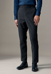 Pantaloni su misura neri con design a parte anteriore piatta, texture liscia e vestibilità slim. Abbinati a scarpe eleganti in pelle nera.
