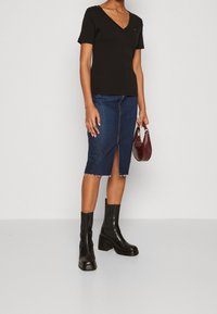 Svart kortärmad t-shirt med v-ringning, kombinerad med en knälång denimkjol med en framficka och rå kant, kompletterad med svarta kraftiga klackstövlar.