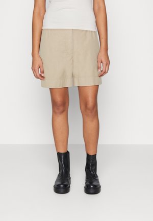 Vaaleat beige-shortsit suoran leikkauksen omaavina, kevyestä kankaasta valmistettuina, yksinkertaisella helman viimeistelyllä, yhdistetty mustiin nilkkasaappaisiin.