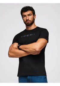 Sort bomulds T-shirt med flerfarvet tekst "cantire" henover brystet, korte ærmer og en tætsiddende design.