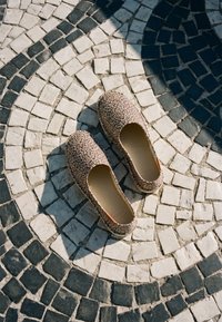 Paire de chaussures slip-on à imprimé léopard posée sur un pavement circulaire en mosaïque noir et blanc avec lumière du soleil et ombre.