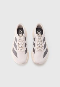 Jasnoróżowe buty sportowe z szarymi akcentami i trzema białymi paskami. Charakteryzują się smukłym designem, zaokrąglonym noskiem i sznurowanym zapięciem.