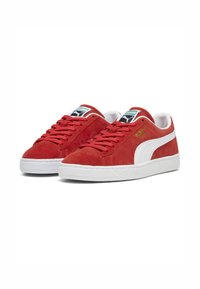 Røde ruskinds sneakers med hvide gummisåler, med en hvid side-stribe og logo på tungen. Flade snørebånd og tekstureret detaljering.
